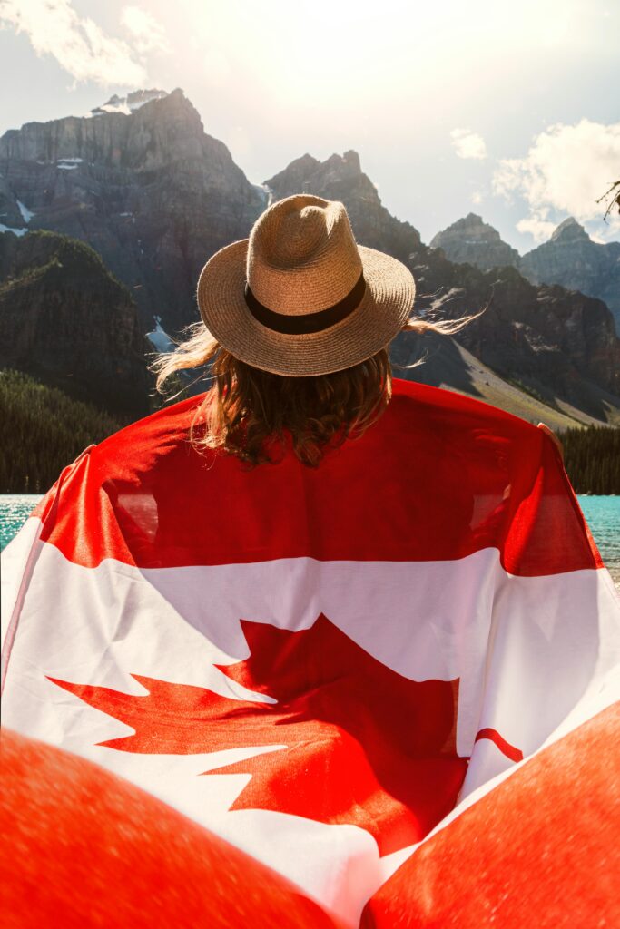 A person draped in a Canadian flag sitting by Moraine Lake with mountains in the background.